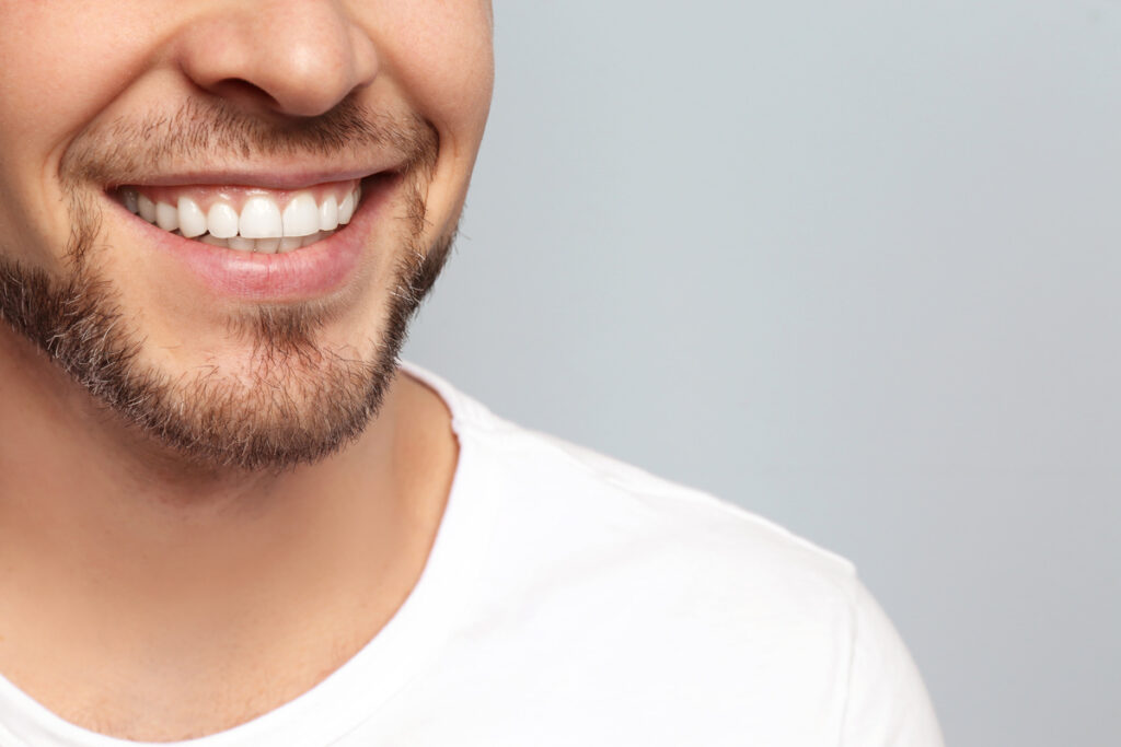 Young man with beautiful smile on grey background. Teeth whiteni