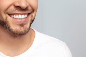 Young man with beautiful smile on grey background. Teeth whiteni