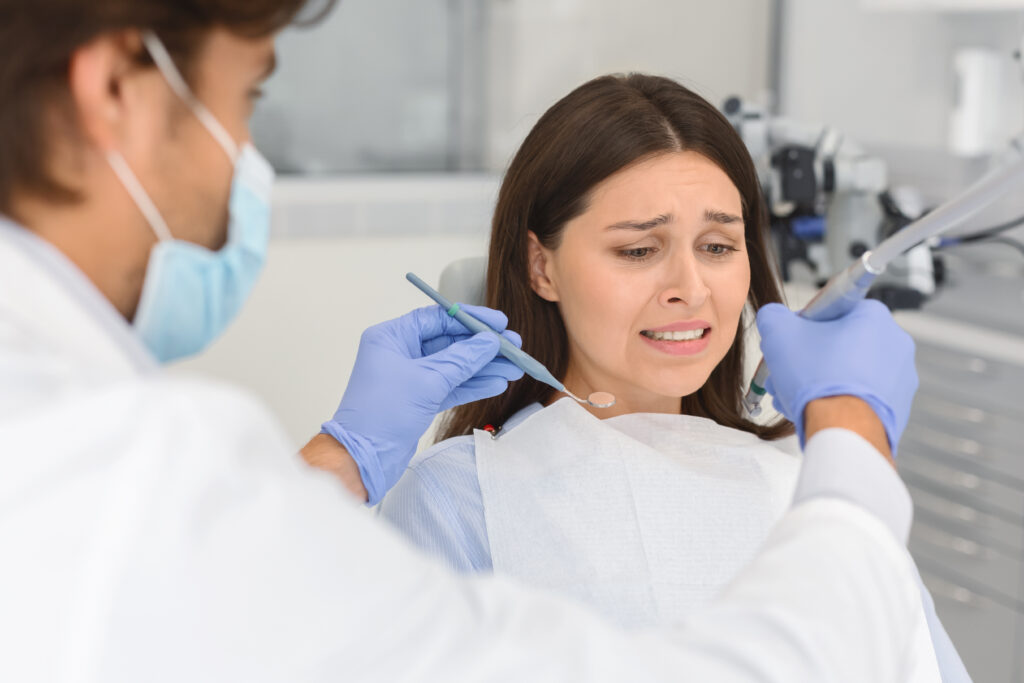 Dentophobia concept. Frightened young woman looking at dental tools in doctor hands