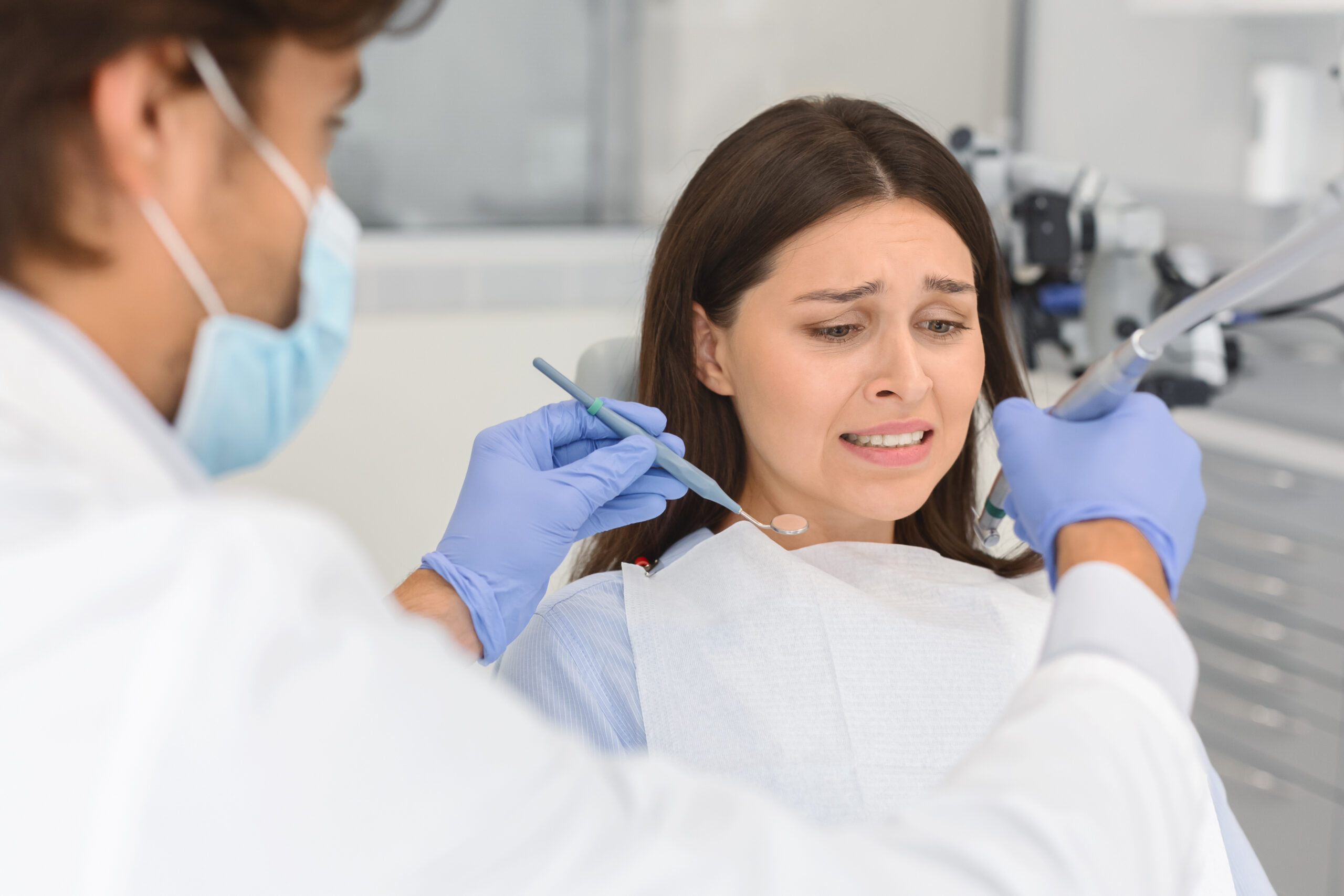 Dentophobia concept. Frightened young woman looking at dental tools in doctor hands