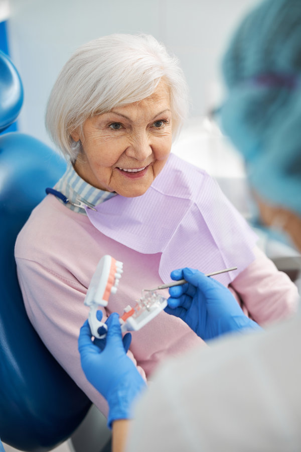 Curious retired woman staring at a dental professional while she pointing at transparent part of teeth model with probe