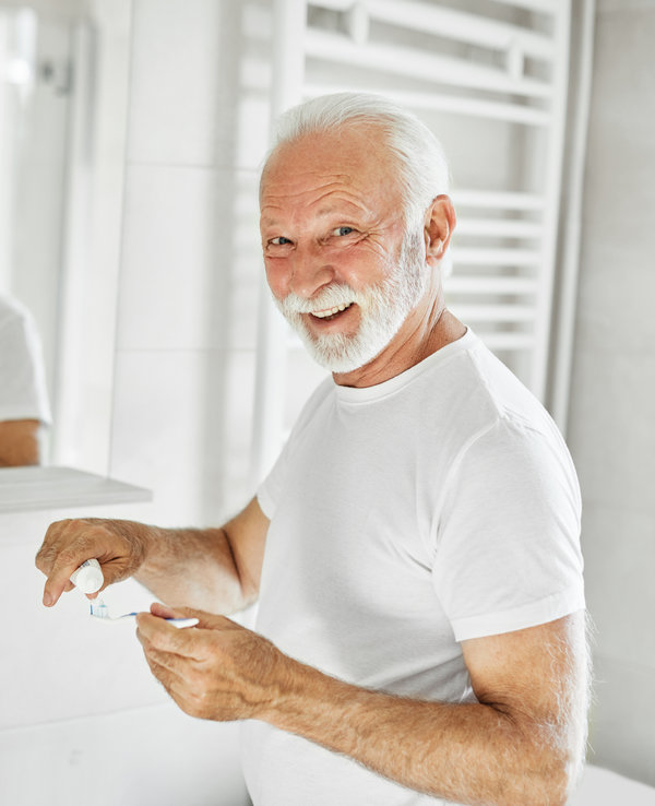 Portrait of an elderly senior man is cleaning brushing his teeth in front of mirror in bathroom. Dental hygiene, vitality and beauty concepts
