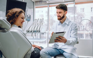 People, medicine, stomatology and health care concept - happy male dentist showing tablet computer to woman patient at dental clinic office.
