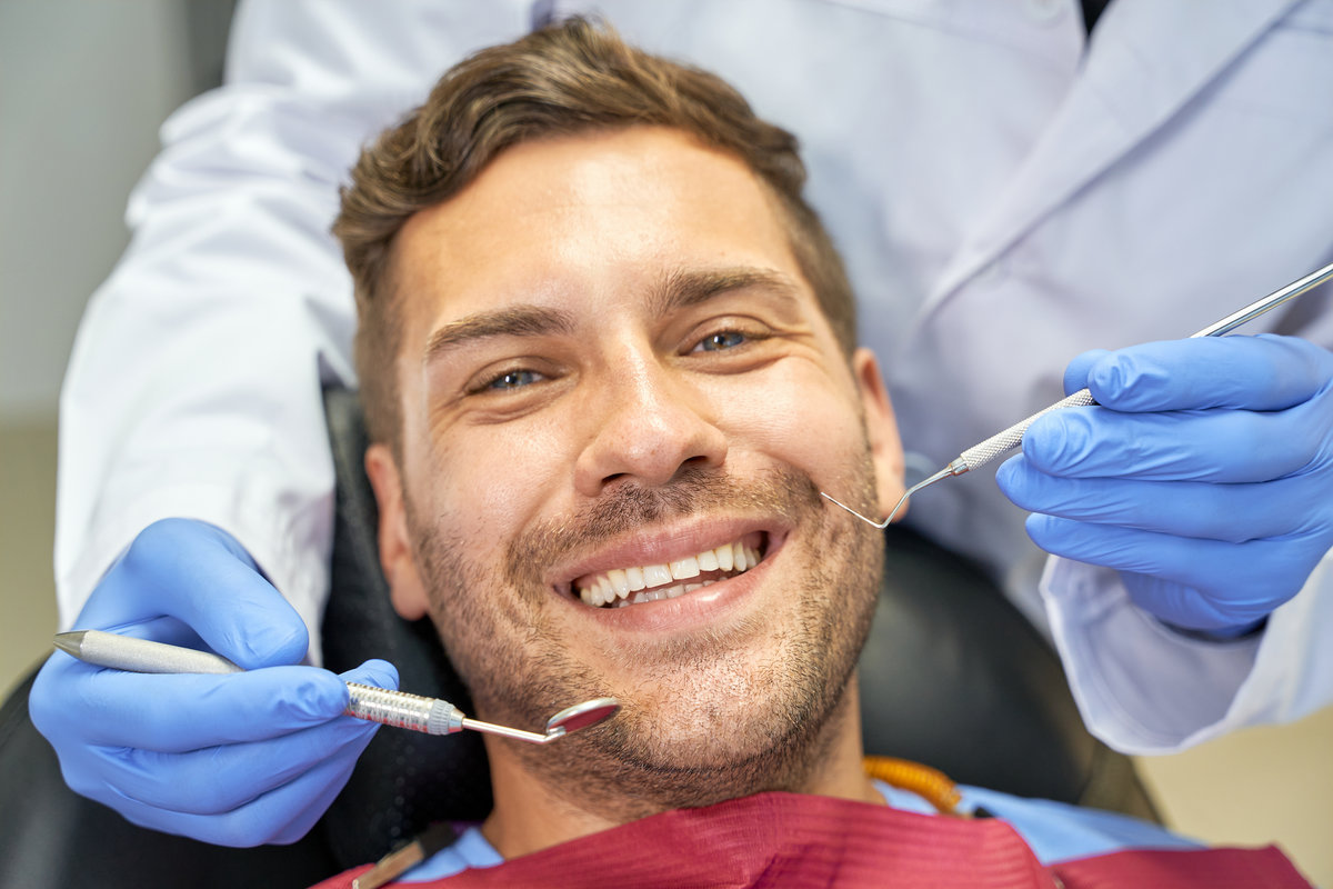 Close-up photo of an amicable young man having dental check-up and looking at the camera
