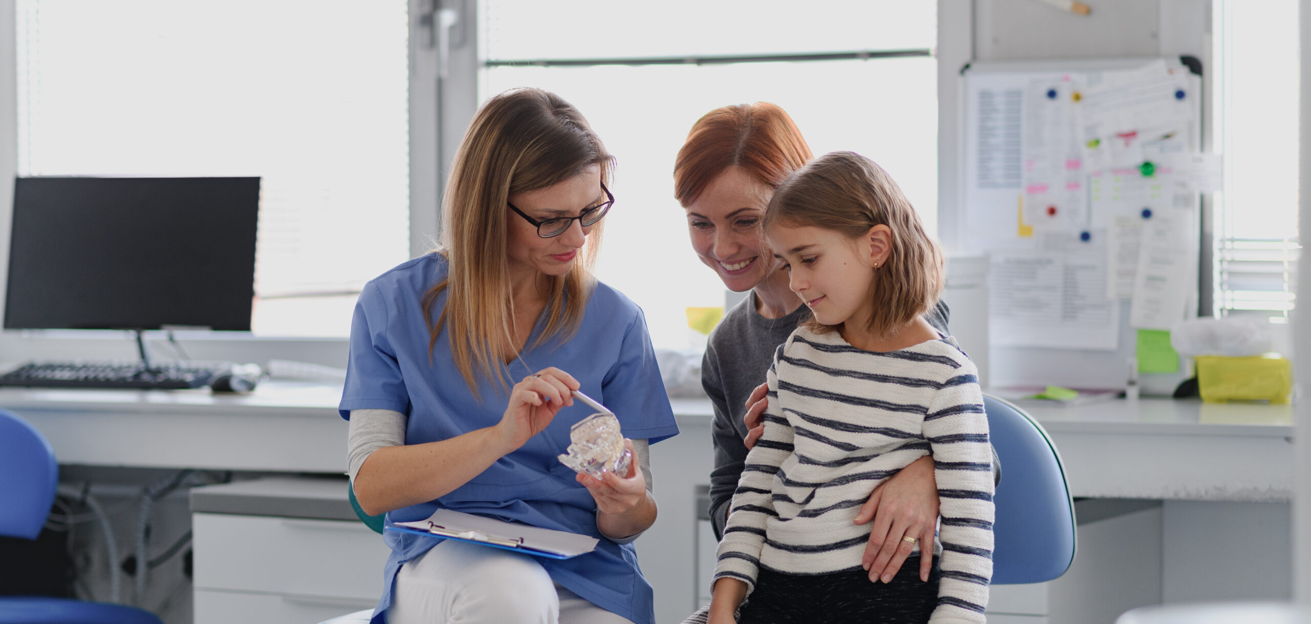Cute girl showing her lost tooth to the dentist during a routine checkup at the dental clinic. Banner with copy space.