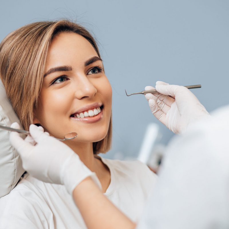 attractive woman with short hair sit in dental office and look at doctor with confidence, she has perfect smile. professional doctor of clinic use special sterilized medical instruments