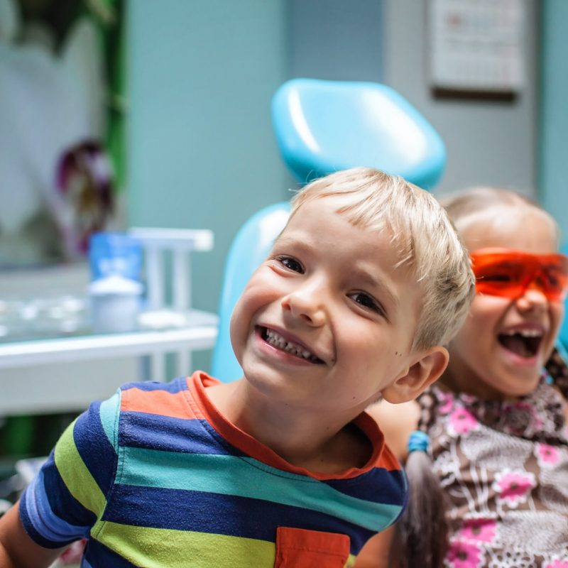 Two kids having fun and wearing medical eyeglasses during their visit to dentist office, the two are not scared. Healthy teeth and painless treatment, pediatric dentistry concept