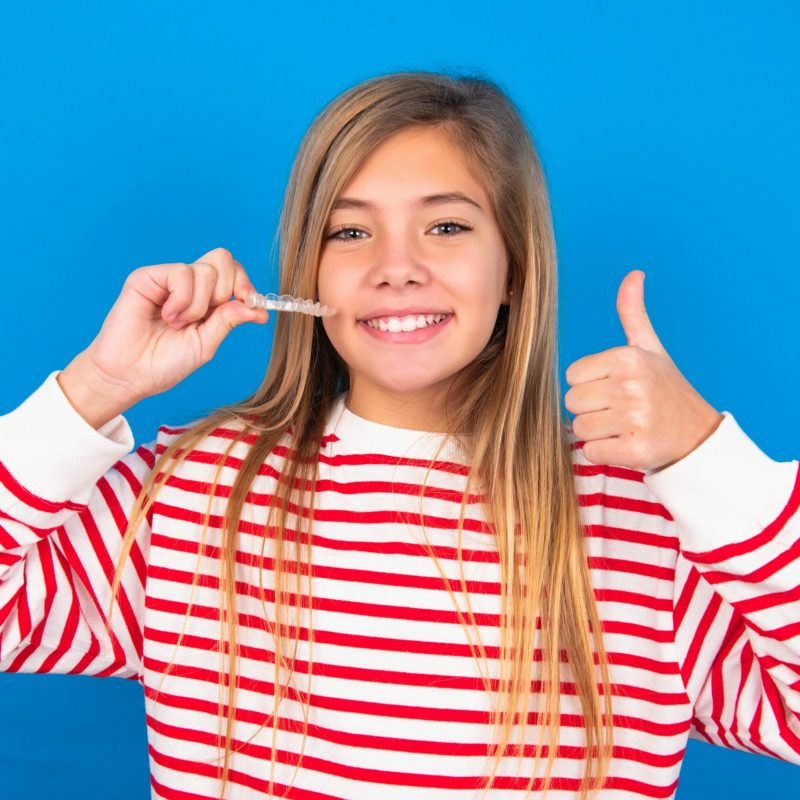 MODEL holding an invisible braces aligner and rising thumb up, recommending this new treatment. Dental healthcare concept.