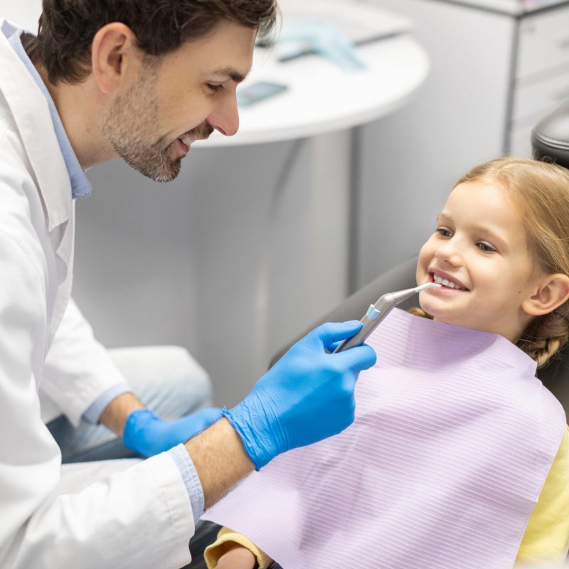 Professional hygiene for child teeth. Male dentist examining and consulting kid girl patient in dentistry clinic office
