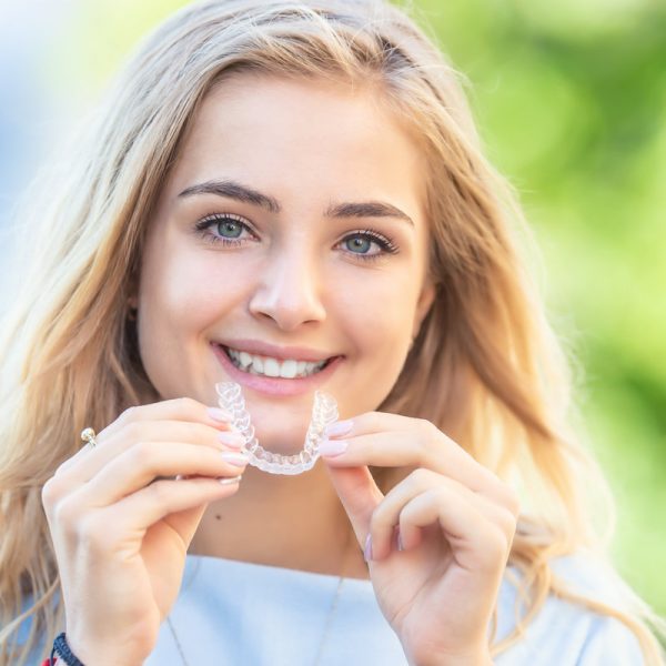 Invisalign orthodontics concept - Young attractive woman holding - using invisible braces or trainer.